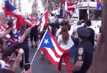 a crowd of people are holding flags and a police officer is standing in the middle of the street .