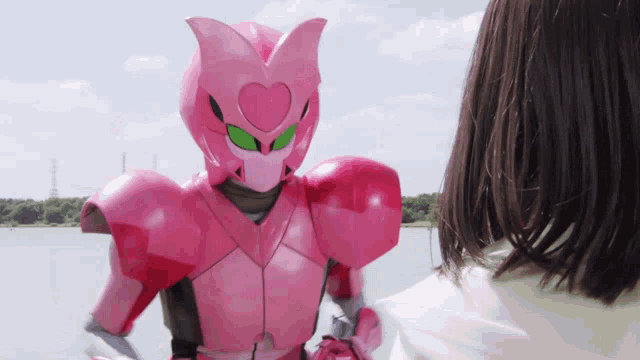 a woman stands next to a pink robot with a heart on its head