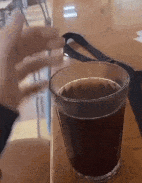 a glass of coffee is sitting on a wooden table next to a cell phone .