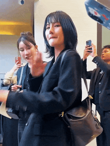 a woman in a black jacket holds a purse and a cell phone