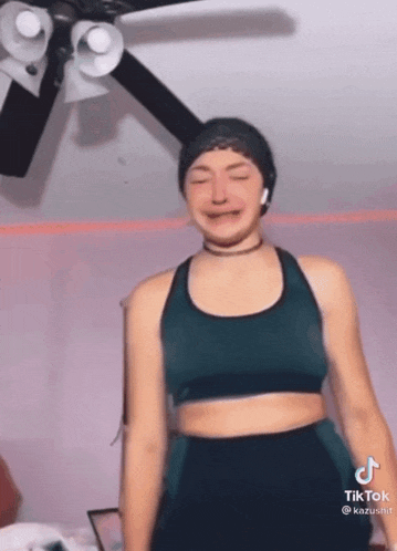 a woman in a green sports bra is dancing in front of a ceiling fan ..