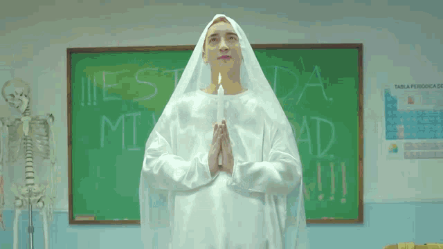 a man in a nun costume holds a candle in front of a chalkboard that says " esta mi edad "