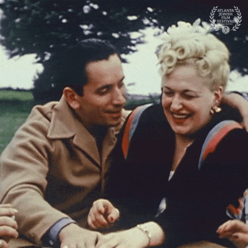 a man and a woman are sitting next to each other with a laurel wreath on the bottom right