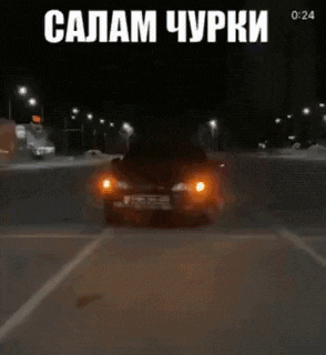 a black car is driving down a street at night with its lights on .