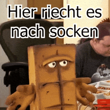 a man sits at a table with a puppet that says hier riecht es nach socken on it
