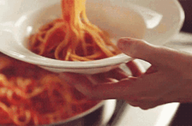 a person pouring spaghetti into a white bowl
