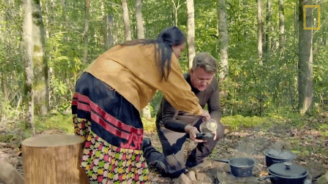 a man and a woman are cooking in the woods