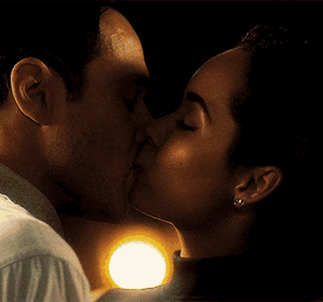 a man and a woman are kissing in the dark with a light behind them