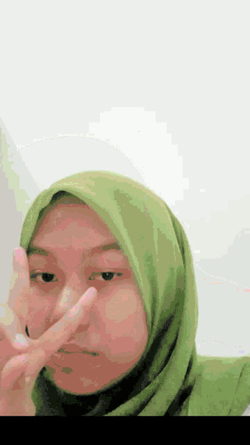 a woman wearing a green hijab is giving a peace sign