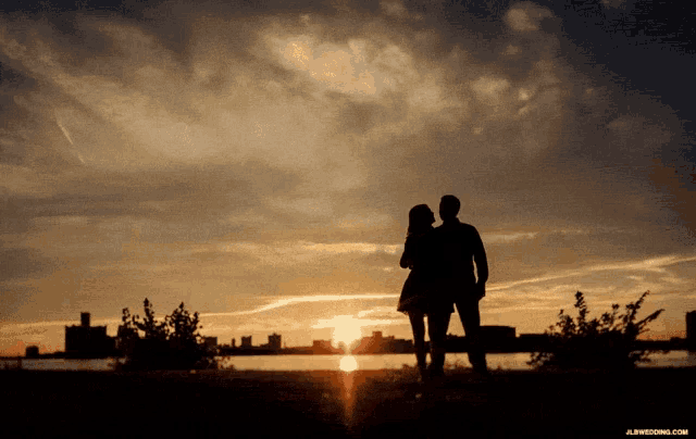a silhouette of a man and a woman looking at the sunset