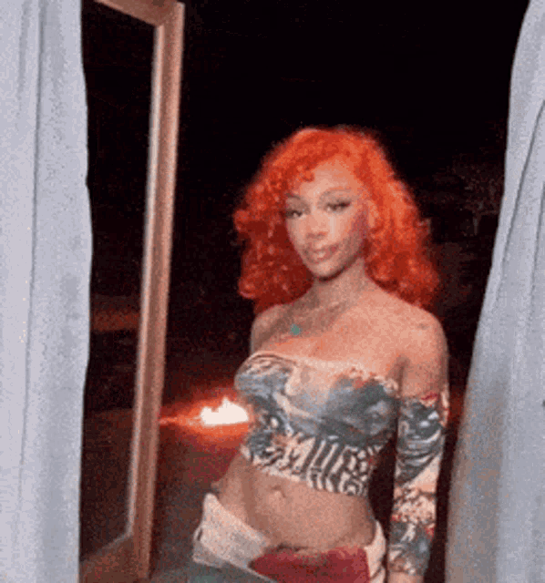a woman with red hair is standing in front of a window in a room .
