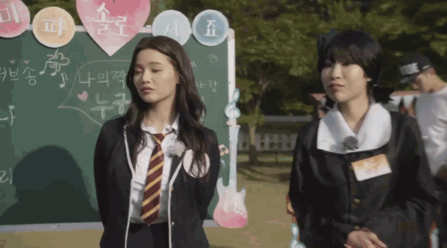 two girls standing in front of a blackboard with korean writing