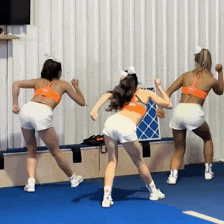 three cheerleaders are dancing on a blue mat in front of a wall .