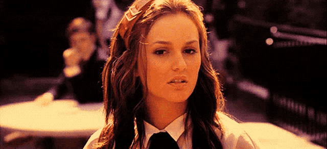 a woman wearing a headband and a tie is sitting at a table looking at the camera .