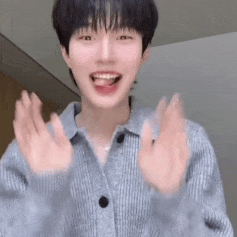 a young man in a sweater is making a funny face with his hands outstretched .