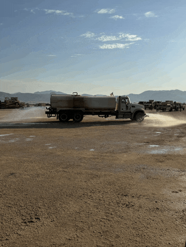 a truck is spraying something in a dirt area with mountains in the background