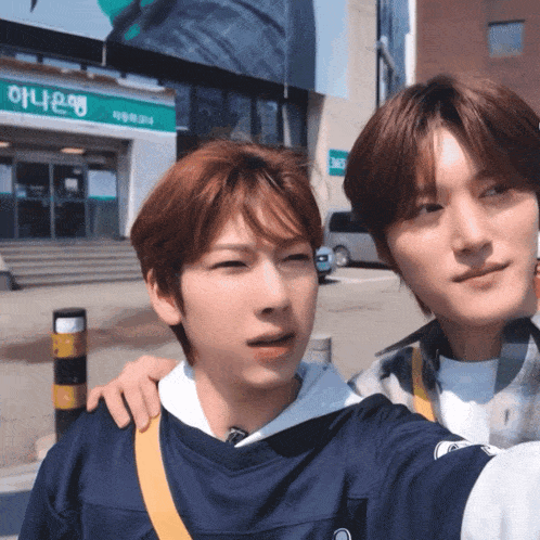 two young men are taking a selfie in front of a building that says ' 하나은행 ' on it