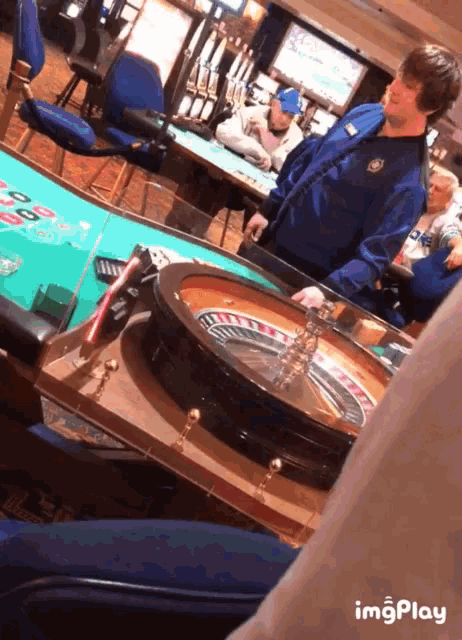 a man in a blue shirt is playing roulette in a casino while another man watches