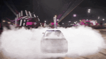 a car is doing a burnout in front of a carnival at night