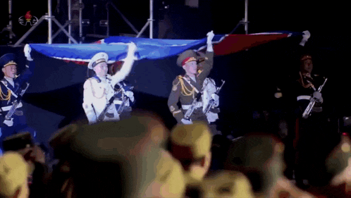 a group of men in military uniforms are holding up a flag in front of a crowd