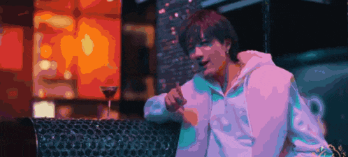 a man in a white hoodie is sitting on a couch with a martini glass in front of him .