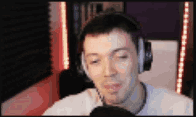 a man wearing headphones is sitting in front of a microphone and looking at the camera .