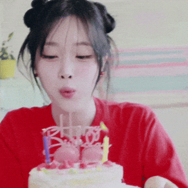 a woman in a red shirt blows out candles on a cake that says " happy birthday "