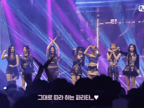 a group of girls standing on a stage with purple lights behind them and a sign that says m