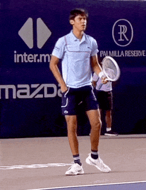 a man holding a tennis racquet on a tennis court in front of a mazda sign