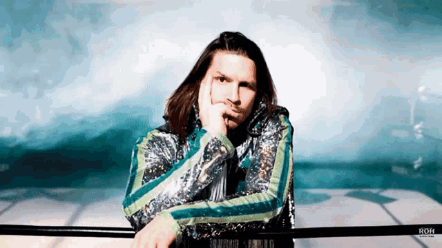a man in a sequined jacket is leaning on a railing with the word roh on the bottom right