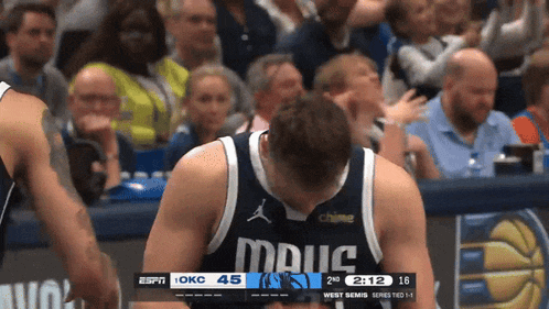 a basketball player wearing a mavs jersey looks down at the scoreboard