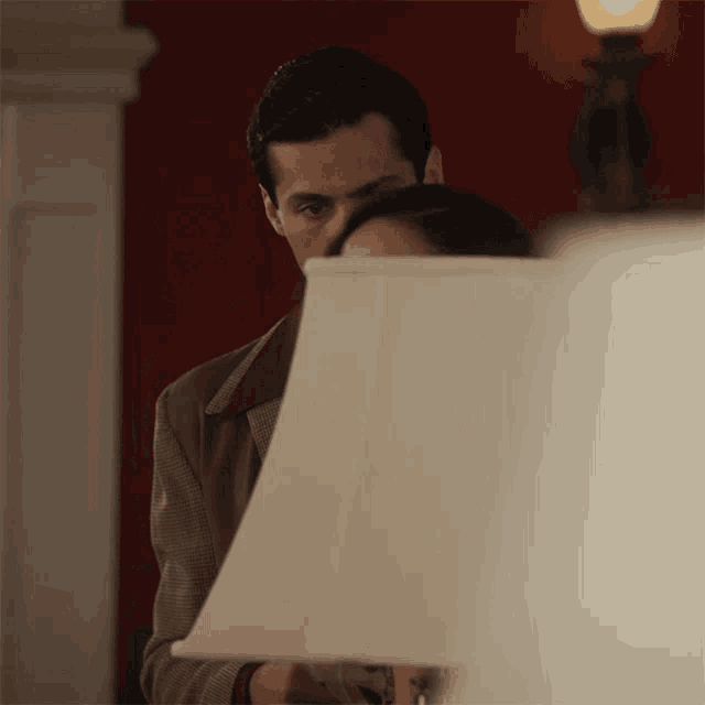 a man and a woman are peeking out from behind a lamp