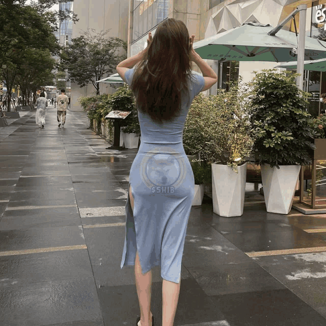 a woman in a blue dress is walking down a sidewalk with a sign that says sshiba