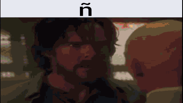 a man with a beard is looking at another man with the letters ñ on the bottom