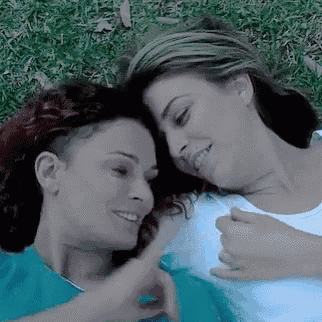 two women are laying on top of each other in the grass and smiling .