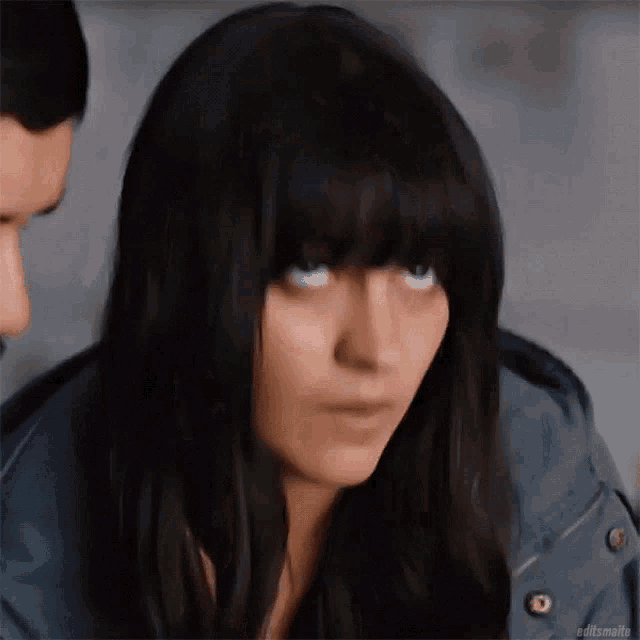 a woman with long black hair and bangs is looking at a man