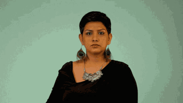 a woman wearing peacock feather earrings has her eyes closed and her hand on her forehead