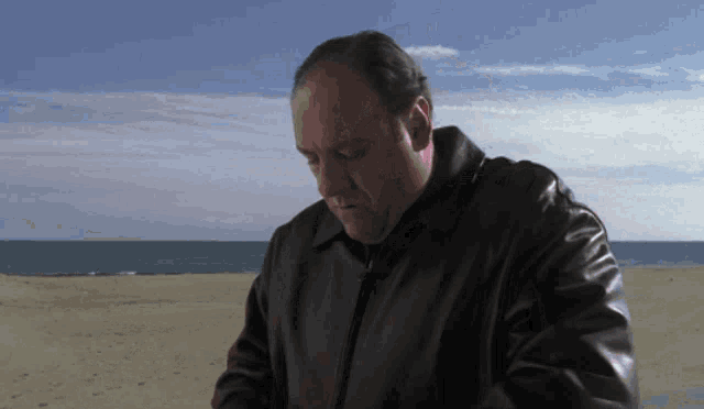 a man in a leather jacket is standing on the beach