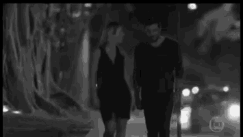 a black and white photo of a man and a woman walking down a street at night .