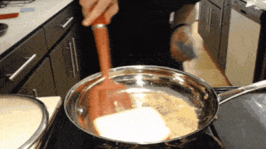 a person is stirring a pan with a red spatula