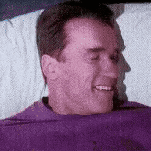 a man in a purple shirt is smiling while laying in bed