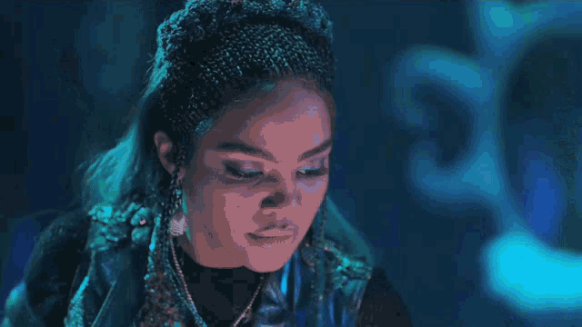 a woman with dreadlocks is standing in a dark room with a blue background