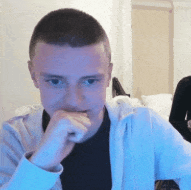 a man wearing a white hoodie and a black shirt has his hand on his chin