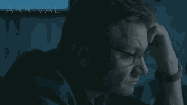 a man with glasses is looking at a screen with the word arrival on it