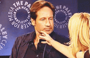 a woman is touching a man 's face in front of a logo for the paley center for media