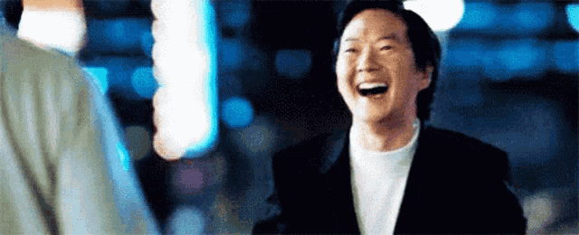 a man in a suit is laughing while talking to another man in a dark room .