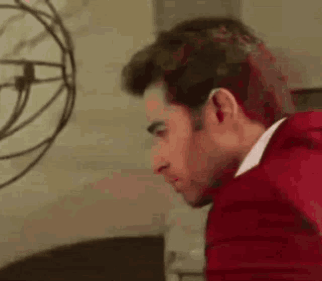 a man in a red jacket and white shirt is sitting in a chair .