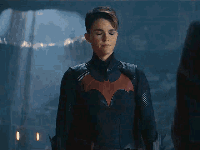 a woman in a black suit with a red bat on the chest