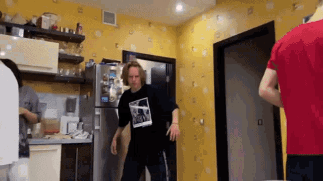 a man in a black shirt with a picture of a man on it stands in a kitchen