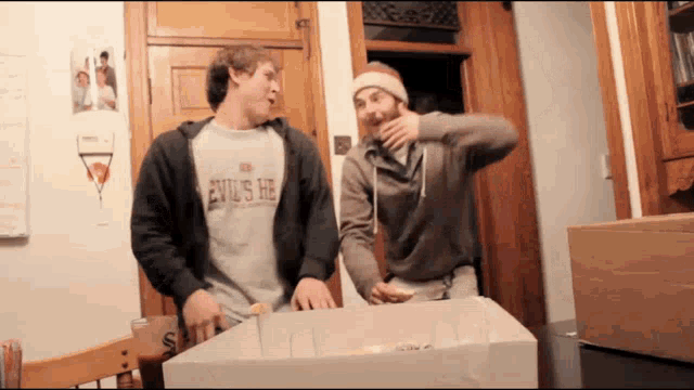 a man wearing an evil 's he shirt is standing next to another man in a room